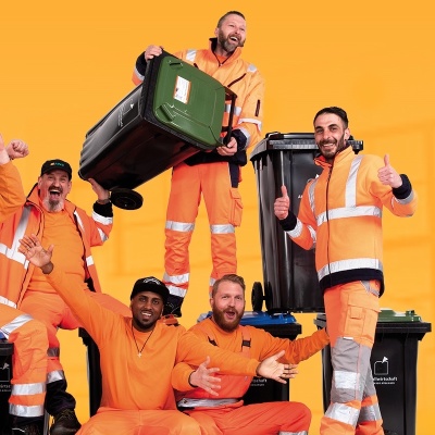 Fröhliche Männer in orangener Arbreitskleidung und Mülltonnen